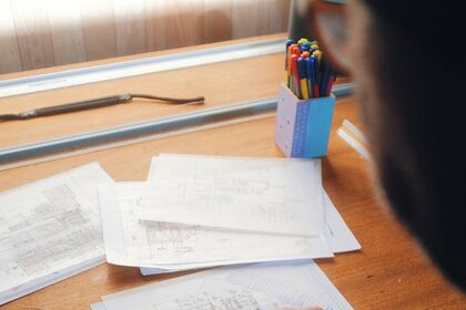 Personne annotant des documents sur un bureau en bois clair.